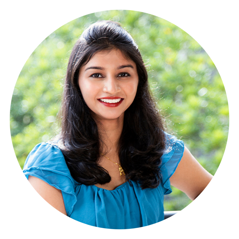 Portrait d’une femme aux cheveux longs, sourire, blouse bleue, en extérieur, fond vert flou.